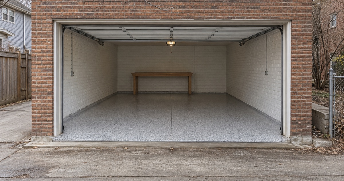 A finished satin gray flake floor in an Oak Park coach-house garage, seen through the open overhead door from the alley.